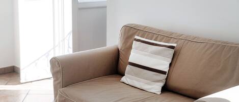 En beige sofa med en stribet pude i et rum med en hvid dør og et vindue.