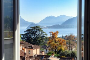 Ein See mit Bergen im Hintergrund, ein Baum mit Herbstlaub und ein Gebäude mit Ziegeldach.