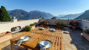 A rooftop terrace with a wooden table set for dining, potted plants, and a scenic mountain view.