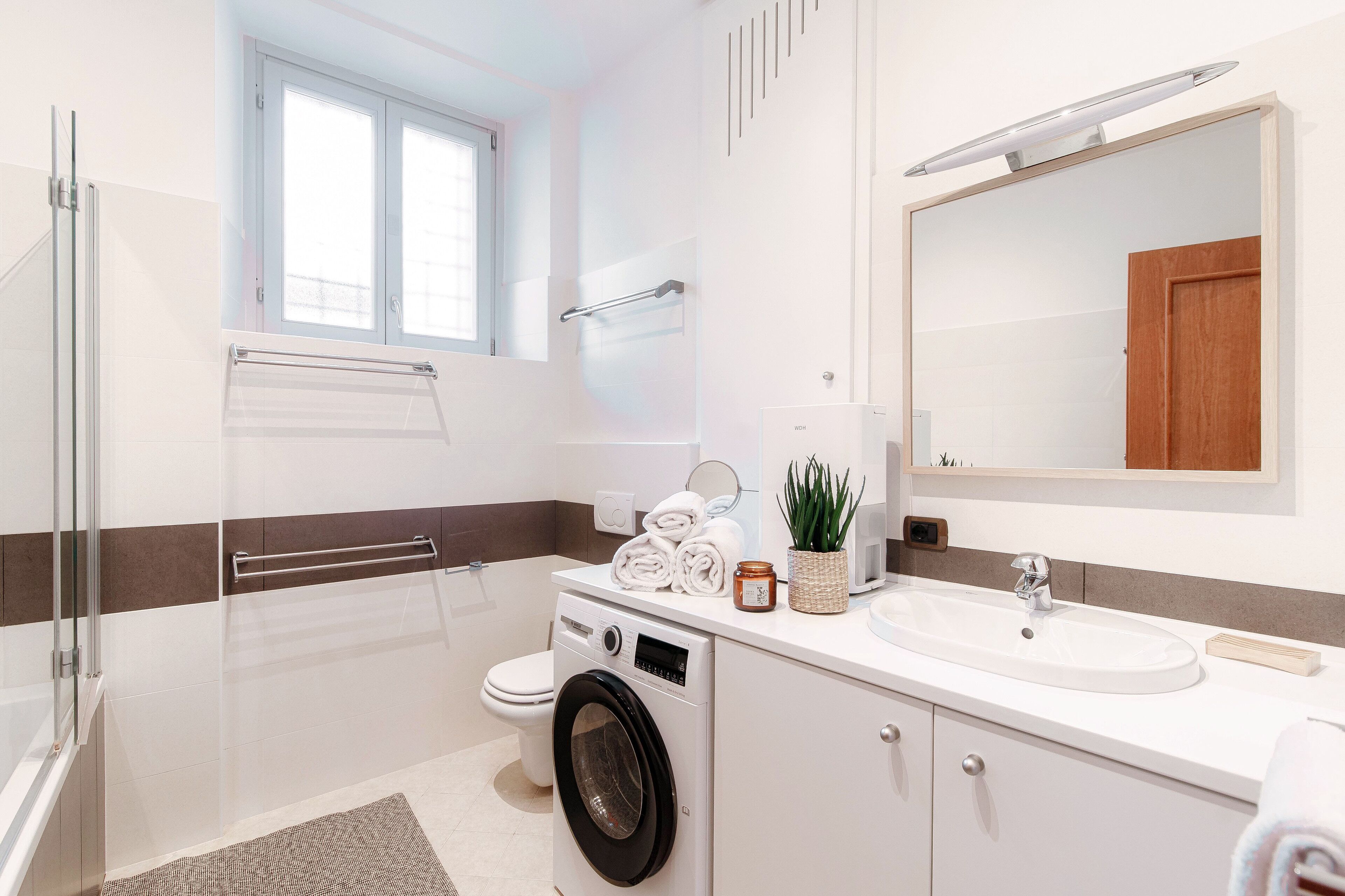 Une salle de bain moderne équipée d’un lave-linge, de toilettes, d’un lavabo et d’un grand miroir.