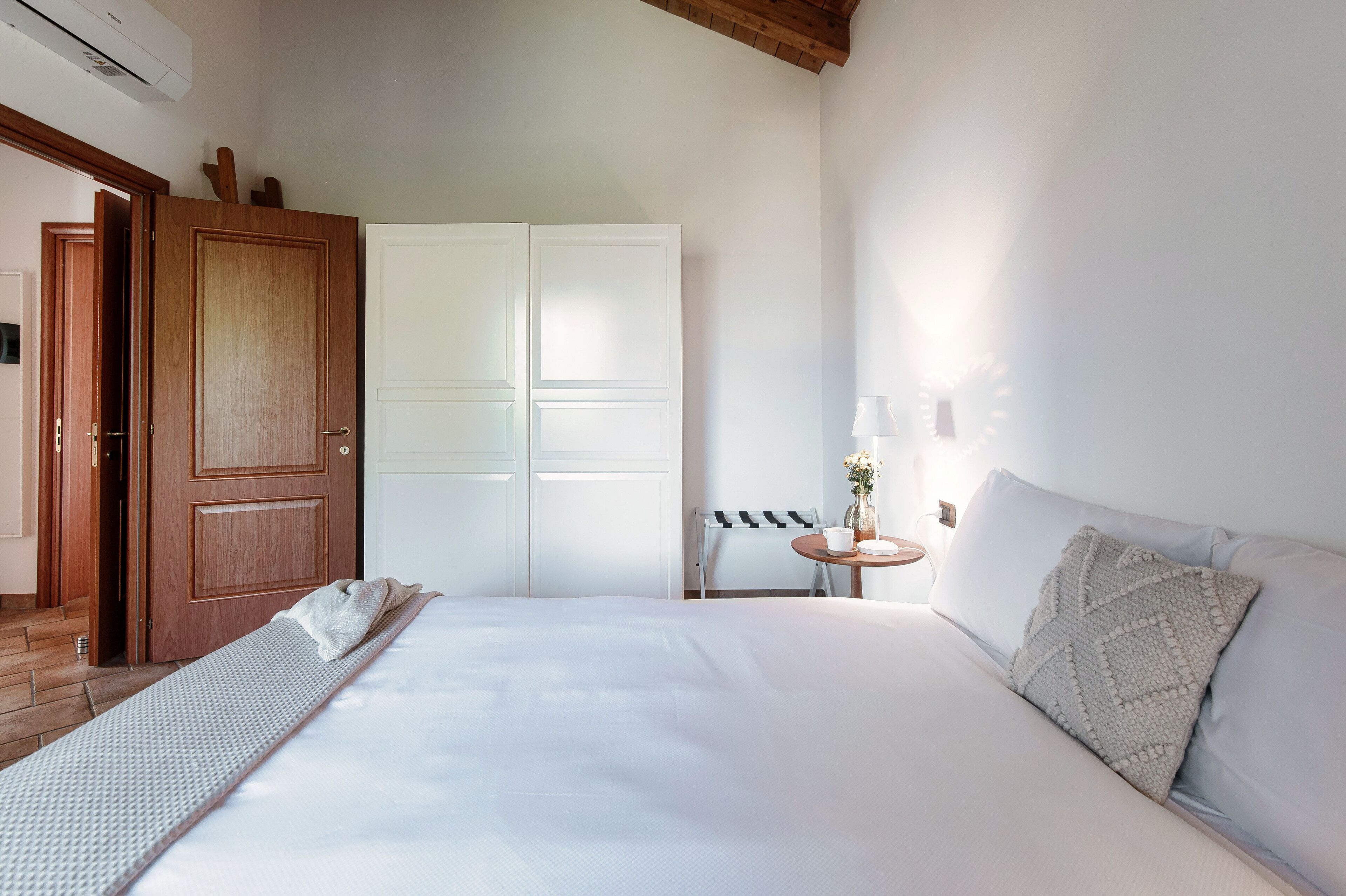Habitación de hotel con una cama grande, un armario de madera, una mesita de noche con una lámpara y una silla.