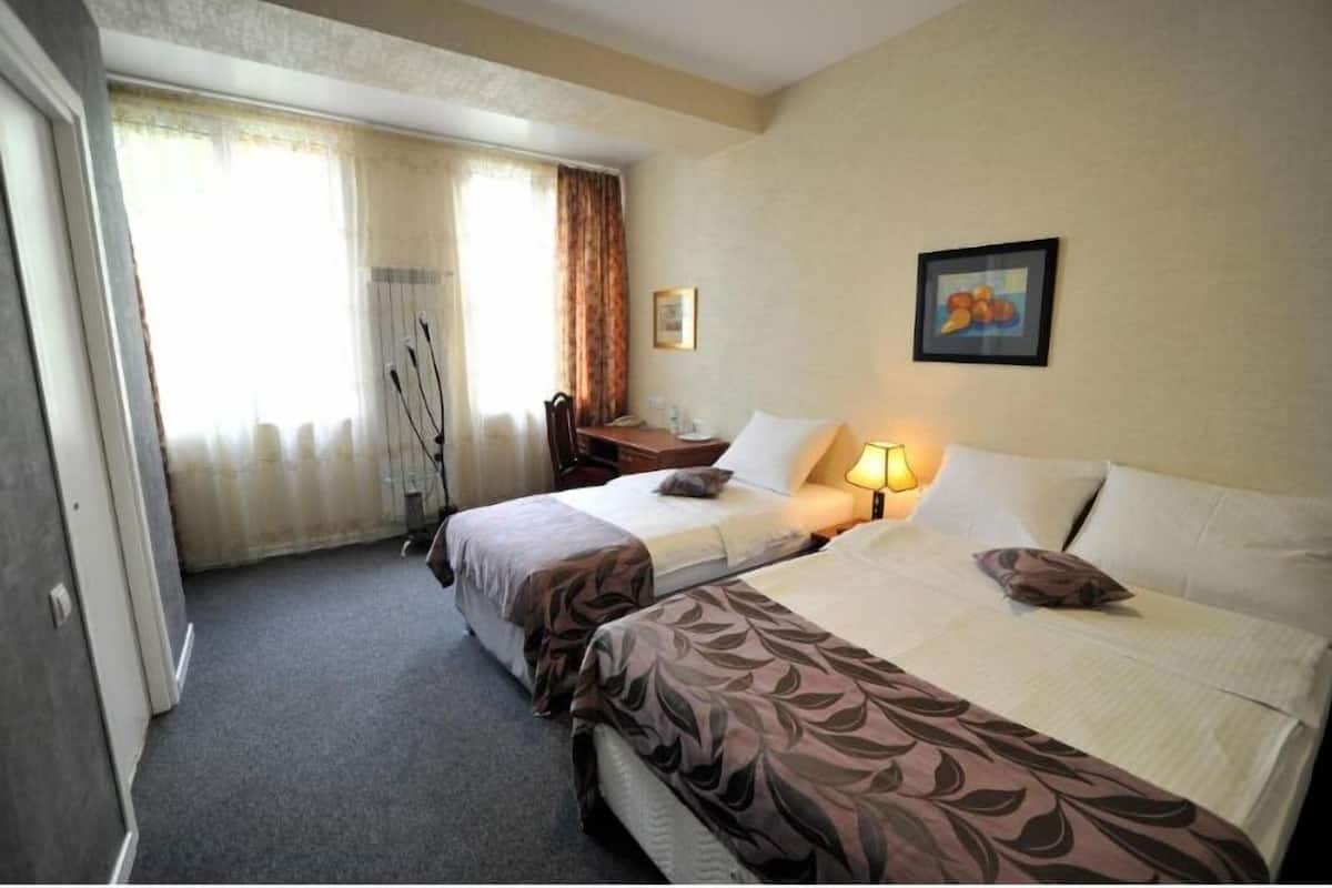 A hotel room with two beds, a desk, a chair, a lamp, and a window with curtains.