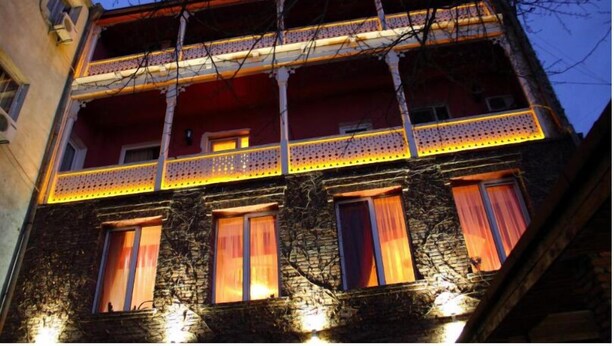 Un edificio a più piani con un balcone, facciata in pietra e diverse finestre con tende.
