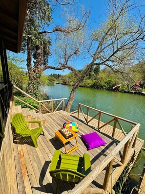 A wooden deck with green chairs and a small table, overlooking a calm river and lush greenery. - Ağva Saklı Bahçe Otel (Sile)