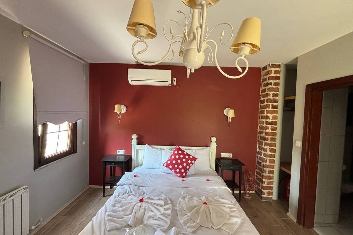 A hotel room with a bed, a chandelier, a brick column, and a window.