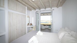 Une chambre à coucher avec un grand lit, une armoire en bois, un bureau avec une chaise et une vue sur l’extérieur, grâce à une porte ouverte.