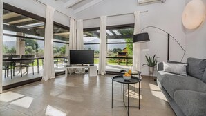 Un vaste espace de vie comprenant un téléviseur à écran plat, un canapé, une table à manger et un balcon offrant une vue sur l’extérieur.