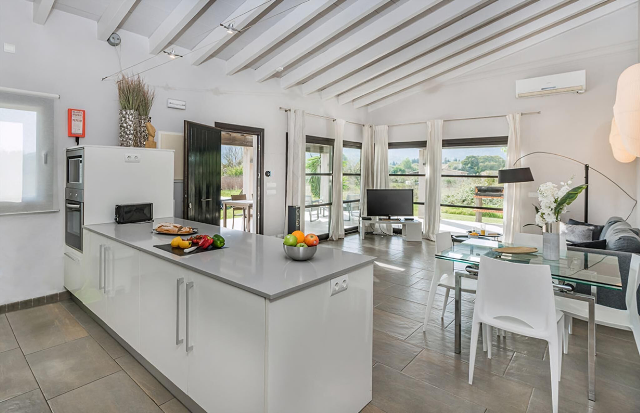 A modern kitchen with a central island, a dining area with a glass table, and a TV in the living area.