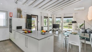 Une cuisine moderne avec un îlot central, un coin repas doté d’une table en verre et un téléviseur dans l’espace de vie.