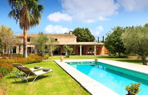 A two-story house with a swimming pool, a patio with lounge chairs, and a garden with various plants and flowers.