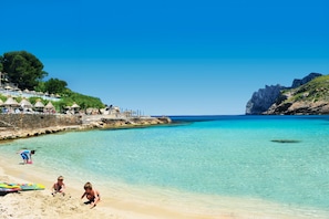 Une plage à l’eau turquoise et limpide, un rivage sablonneux et une falaise rocheuse en arrière-plan.