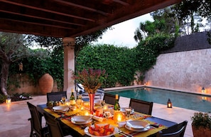 Un espace extérieur aménagé pour les repas, avec une piscine, une pergola en bois et une végétation luxuriante.