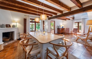 A spacious dining area with a wooden table and chairs, a fireplace, and large windows allowing natural light.