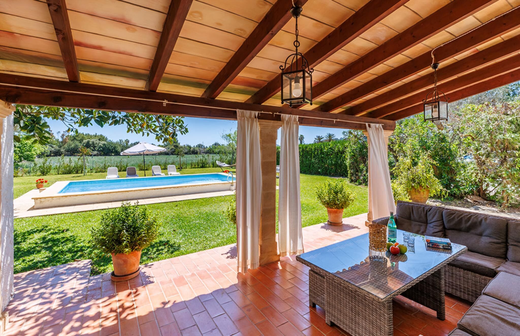 A covered patio with a pool, outdoor furniture, and potted plants.