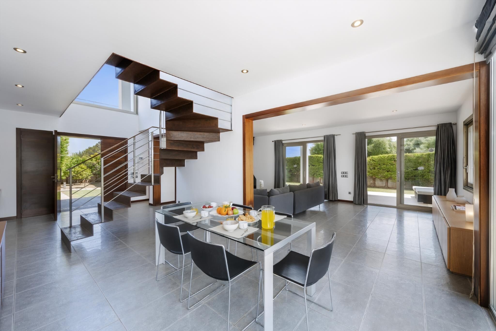 Un interior moderno con comedor, escalera y ventanas amplias.