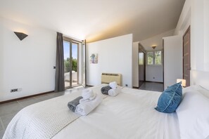A modern hotel room with a large bed, a view through a sliding glass door, and a ceiling fan.