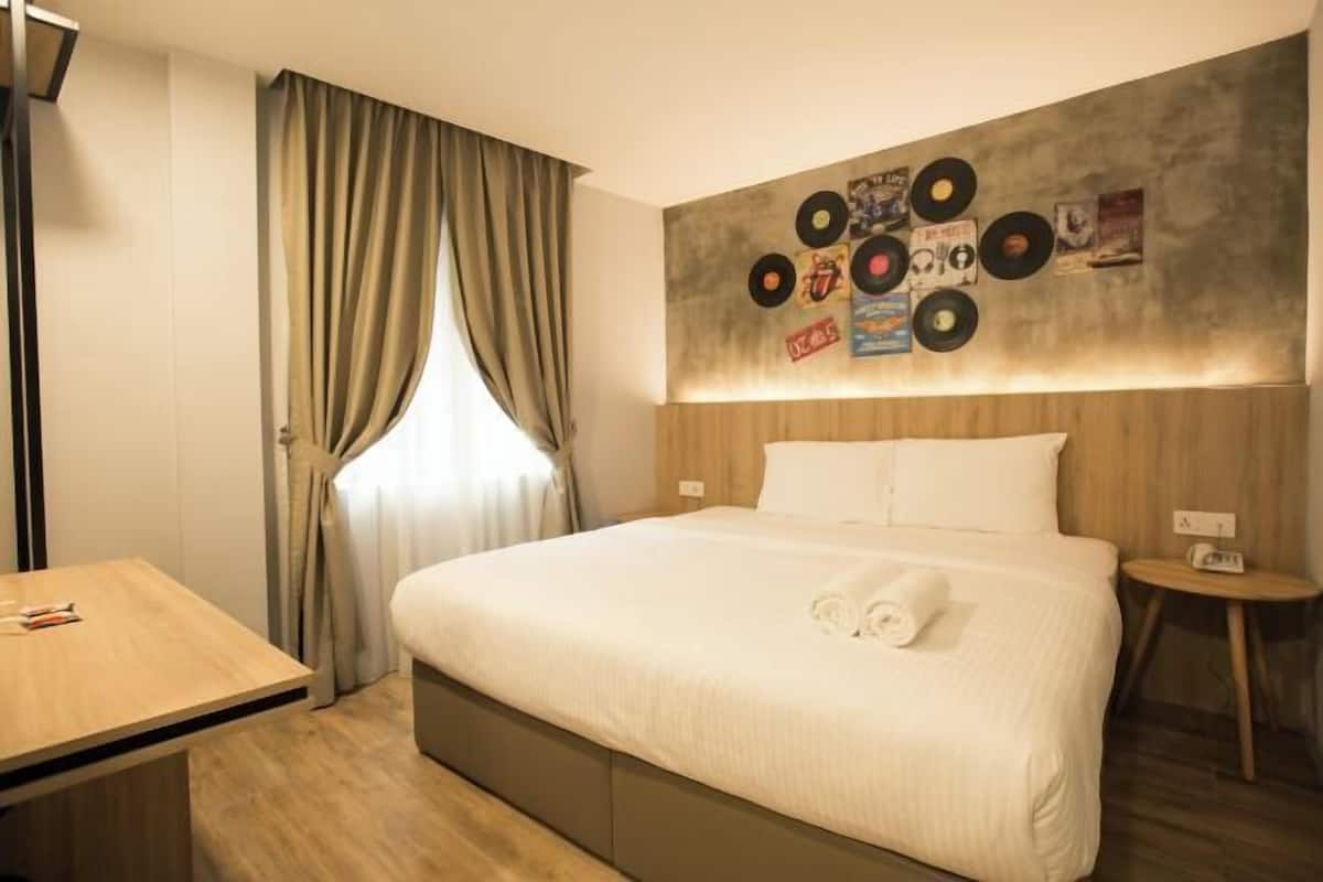 Ein Hotelzimmer mit einem Bett, einem kleinen Tisch, einem Nachttisch, einem Fenster mit Vorhängen und einer Wand, die mit Schallplatten verziert ist.