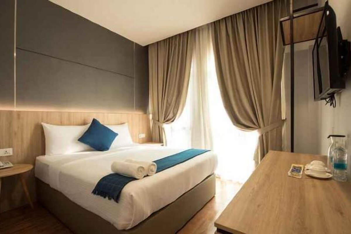 A hotel room with a bed, bedside table, and a TV mounted on the wall.
