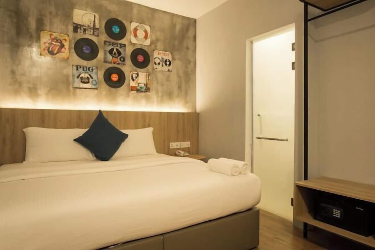 Ein ordentlich bezogenes Bett mit Kissen, eine Wand mit verschiedenen Vinylschallplatten, ein Nachttisch mit Telefon und eine Tür rechts.