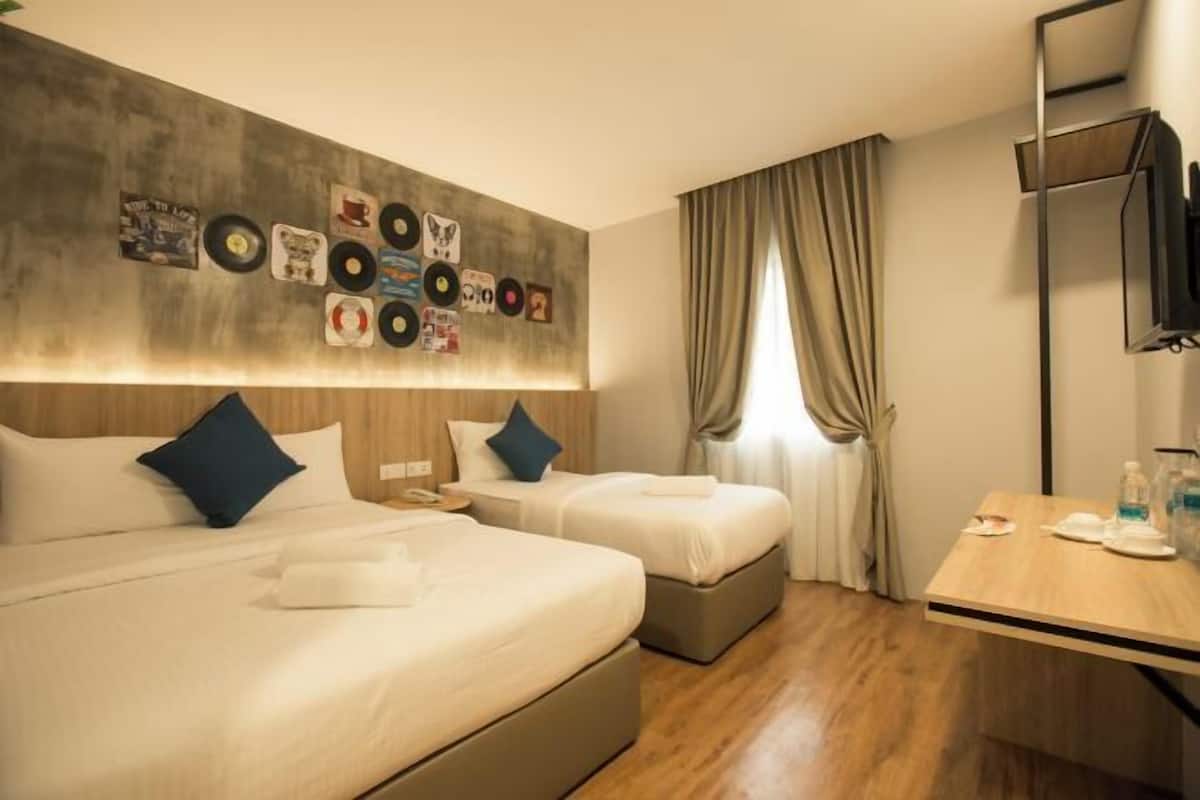 Ein Hotelzimmer mit zwei Betten, einem an der Wand befestigten Fernseher, einem Holztisch und einem Fenster mit Vorhängen.