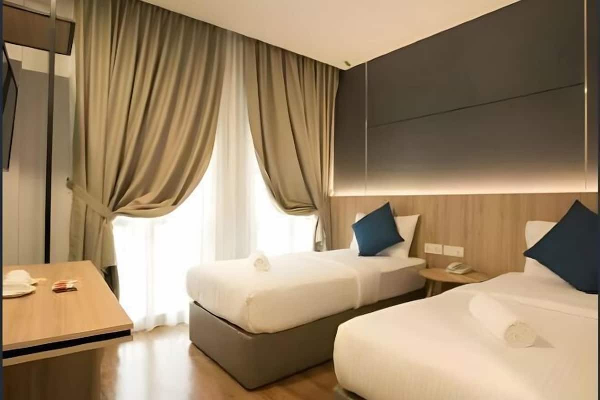 Ein Hotelzimmer mit zwei Betten, einem Holztisch, einem Schreibtisch und einem großen Fenster mit Vorhängen.