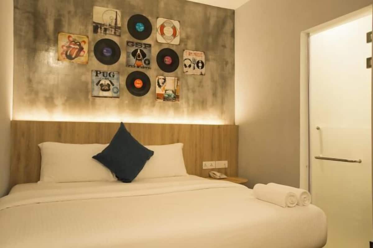 Ein Hotelzimmer mit Bett, Kopfteil, einer Wand mit Schallplatten und einem Nachttisch mit Telefon sowie einer Tür.