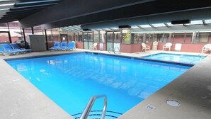 Una piscina interior con agua azul cristalina, rodeada de sillas de descanso y una zona cubierta con ventanales.