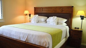 Una cama bien hecha con cabecera de madera, dos lámparas de noche y una mesita de noche con lámpara.
