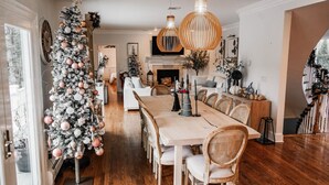 Un comedor amplio con una larga mesa de madera, rodeada de sillas tapizadas. Un gran árbol de Navidad con adornos se encuentra a la izquierda.