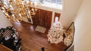Un gran candelabro, un árbol de Navidad blanco y una puerta de madera en un vestíbulo espacioso.