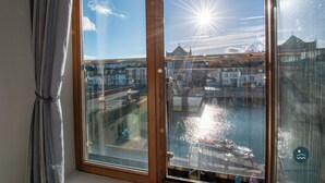 Näkymä ikkunasta, jossa on verho, ja ikkunasta avautuu näkymä vesistöön. Taustalla näkyy vene ja rakennuksia.