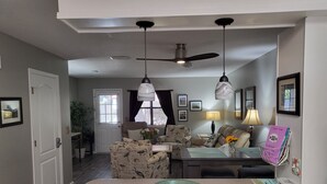 Un salon comprenant un canapé, une table basse et une table à manger. On y trouve également des ventilateurs de plafond, une porte et une fenêtre avec des rideaux.