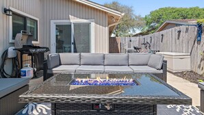 A patio with a glass-top fire pit, a gray sofa, and a grill. - Seascape 55b- Surfer Girl (Miramar Beach)
