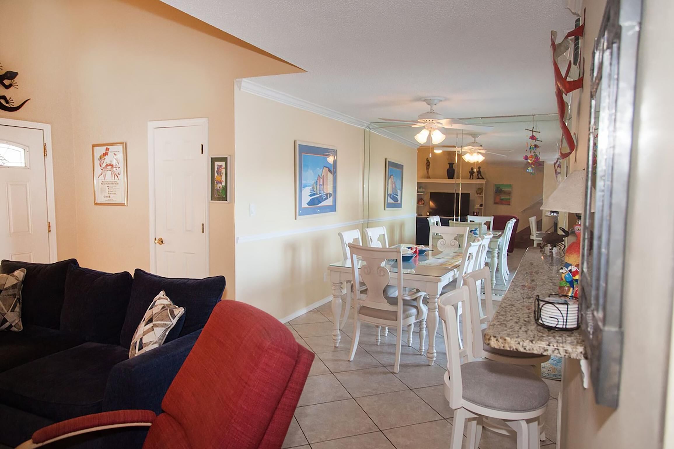 A living room with a dark-colored sofa, a red armchair, and a dining area with white chairs and a table.