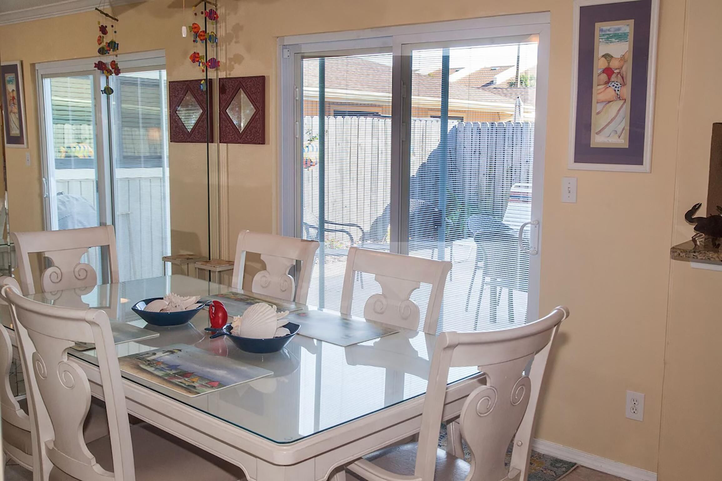 A dining area with a glass-top table, white chairs, and a bowl of fruit.