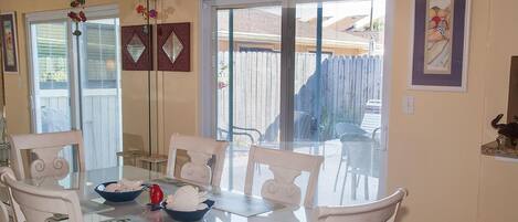 A dining area with a glass-top table, white chairs, and a bowl of fruit.