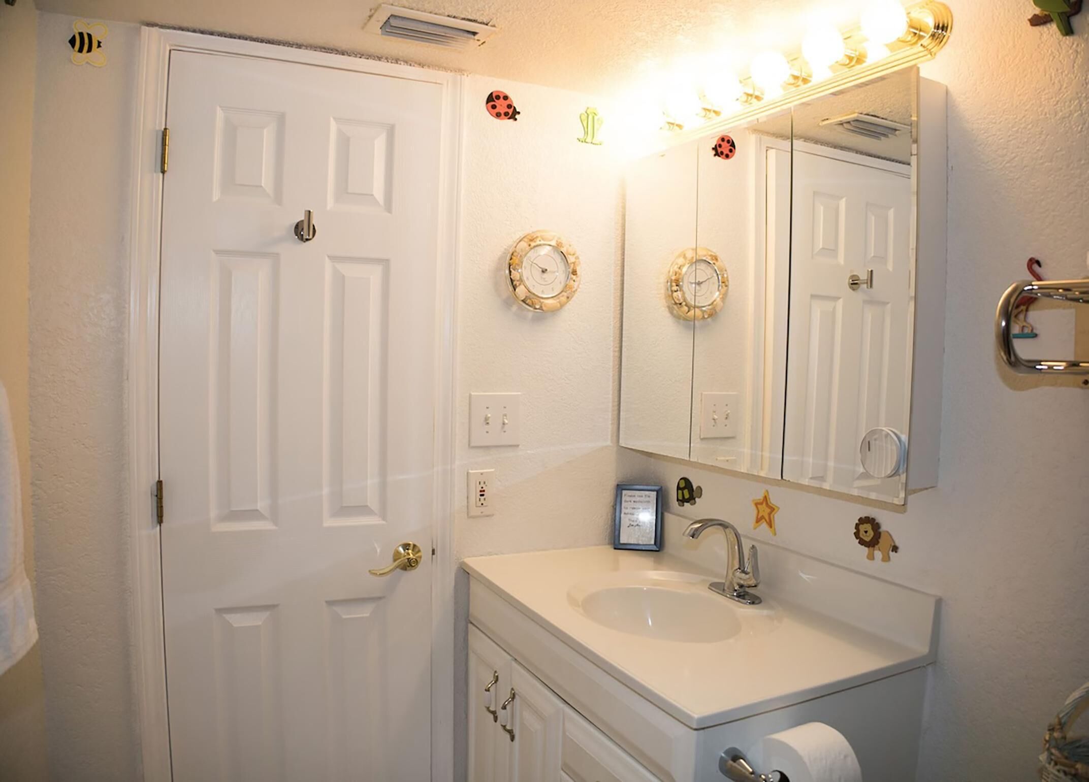 Un bagno con una porta bianca, un lavandino, uno specchio e orologi decorativi a parete.