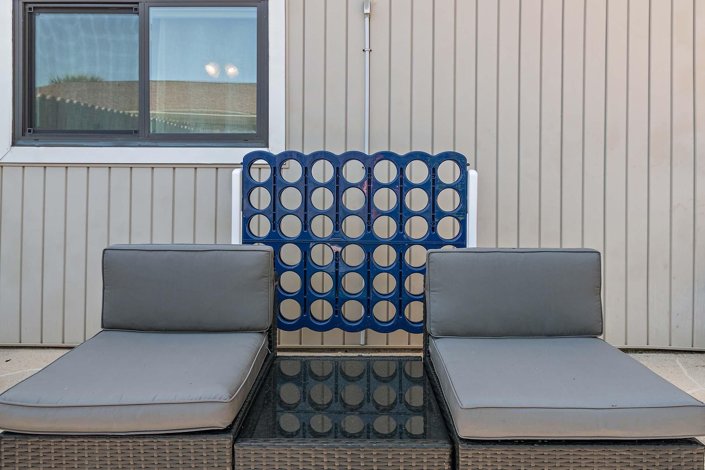 Une chaise longue avec un dossier à motifs bleus et blancs, deux coussins gris et un siège en osier tressé.