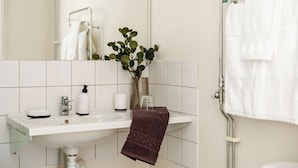 A bathroom with a white sink, a mirror, a towel rack, and a plant. - Hotell Säsong - Boden Business Park (Boden)