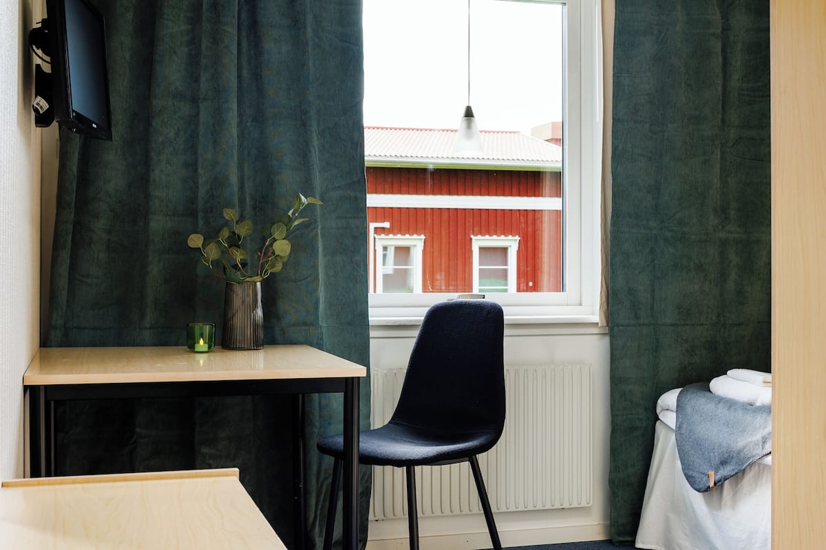 A small room with a desk, chair, and a window with curtains.