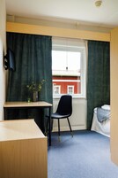 Una habitación pequeña con un escritorio, una silla y un ventanal con cortinas.