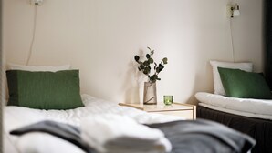 A neatly made bed with white and green bedding, a small bedside table with a green candle, and a vase with green leaves. - Hotell Säsong - Boden Business Park (Boden)
