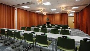 A conference room with a long table, green chairs, and a stage with curtains. - Hotell Säsong - Boden Business Park (Boden)