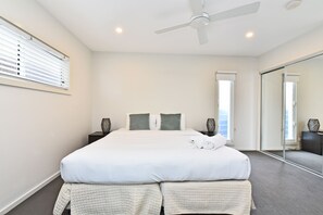 A modern hotel room with a large bed, a ceiling fan, a window with blinds, and a mirror on the wall.