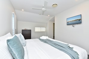 Une chambre à coucher comprenant un lit, un ventilateur de plafond, une fenêtre avec des stores, une porte et un téléviseur fixé au mur qui diffuse une vue panoramique.