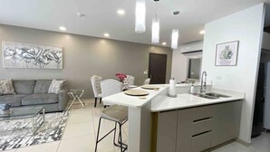 Una cocina moderna con una isla central, iluminación colgante y una zona de comedor con sofá y sillas.
