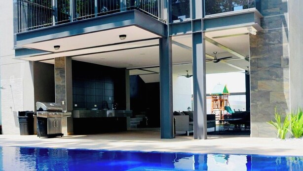 Una casa moderna de dos pisos con un amplio balcón de vidrio, piscina y zona de patio.