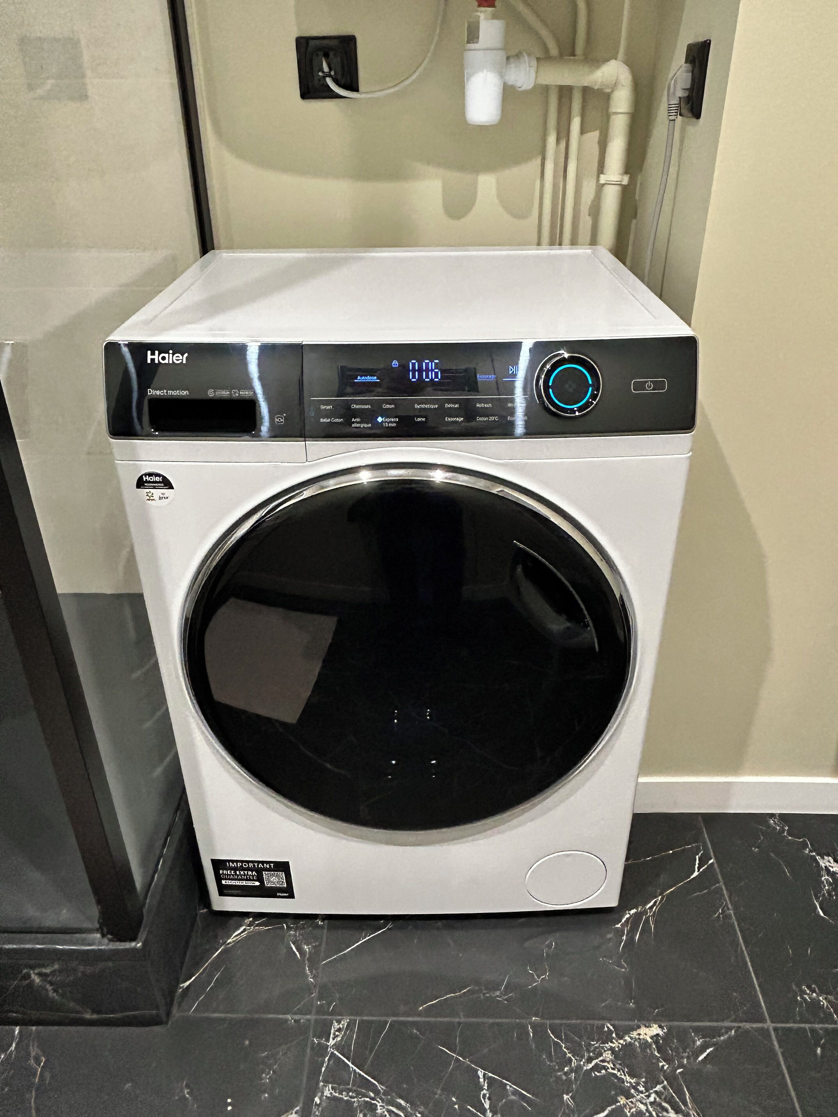 Une machine à laver Haier à entraînement direct, dotée d’un écran numérique, d’un bouton d’alimentation et d’un panneau de commande.