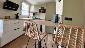 Een moderne keuken met witte kasten, een houten aanrecht en twee rieten stoelen.