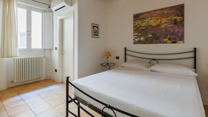 A bedroom with a bed, a radiator, a window with curtains, a small table with a lamp, and a painting on the wall. - Bertiera Family Duplex by Wonderful Italy (Bologna)